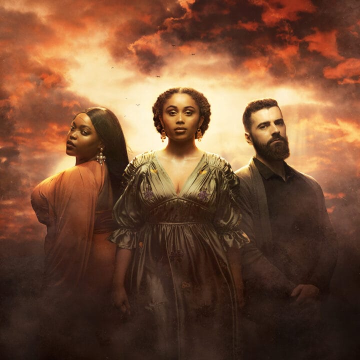 Three members of the cast stand in dramatic lighting against a cloudy, orange-lit sky: two women in ornate dresses, evoking Queen of the Fight, and a bearded man in dark clothing reminiscent of James IV.