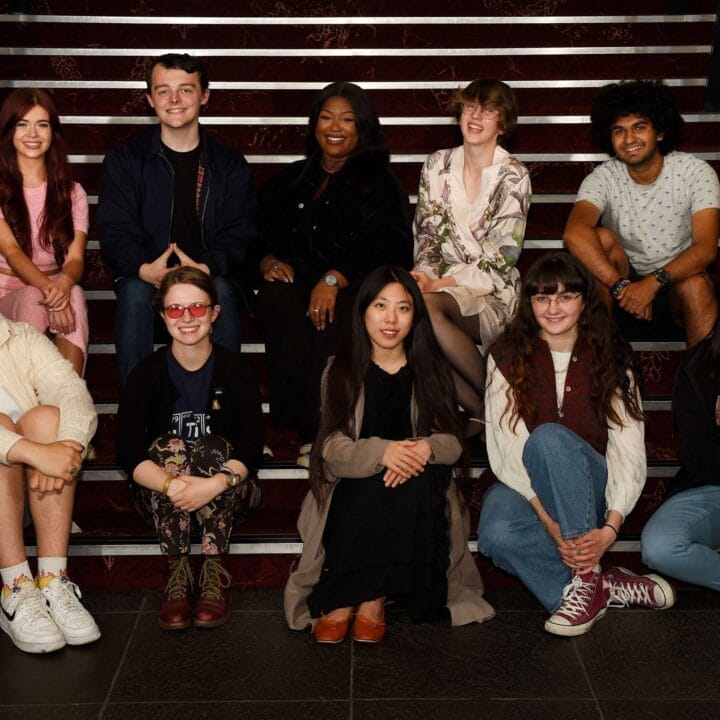 A group of ten people, the Youth Advisory Board, sit and kneel on indoor stairs, posing for a photo.