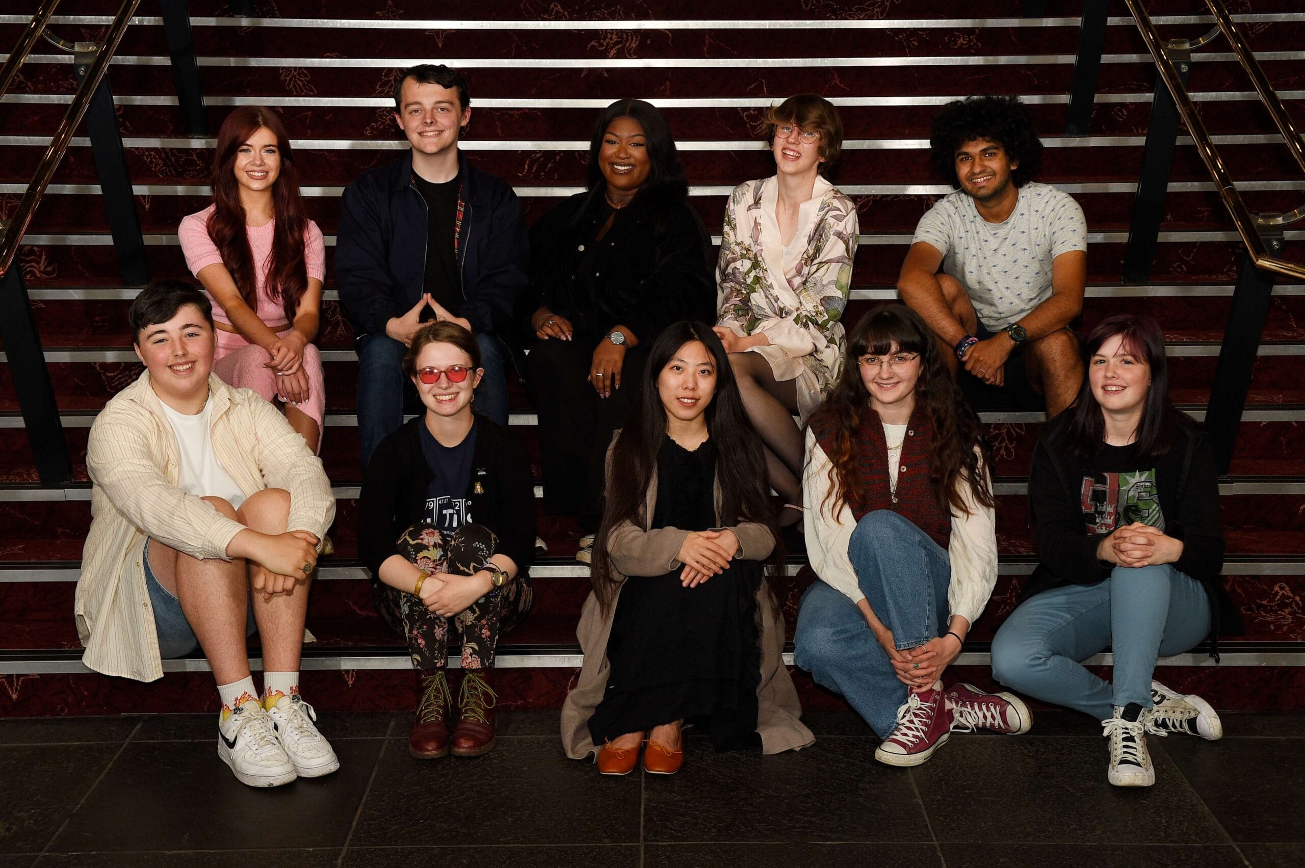 A group of ten people, the Youth Advisory Board, sit and kneel on indoor stairs, posing for a photo.