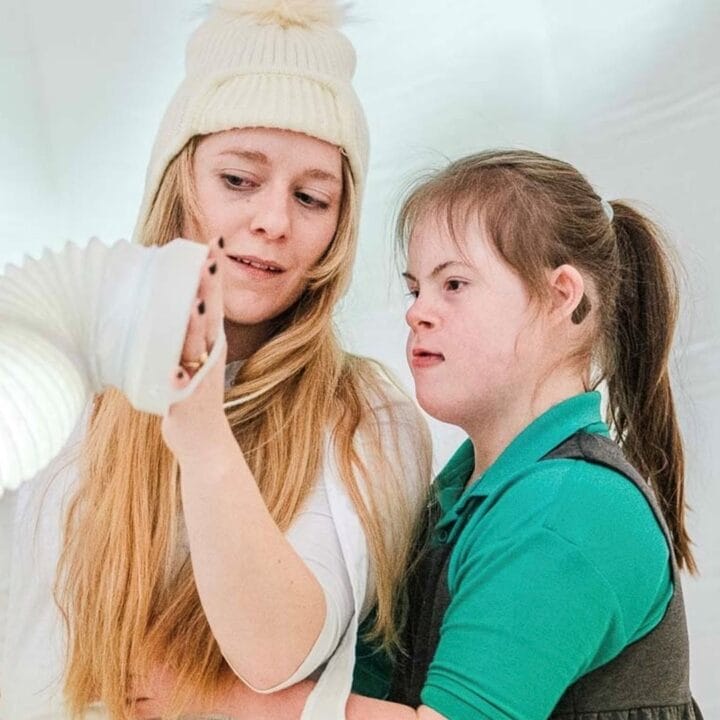 Two girls stand together examining a flexible white light fixture in a bright, white room.