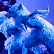 Two dancers in feathered wolf costumes perform on stage under blue lighting, bringing a mystical scene from The Snow Queen to life.