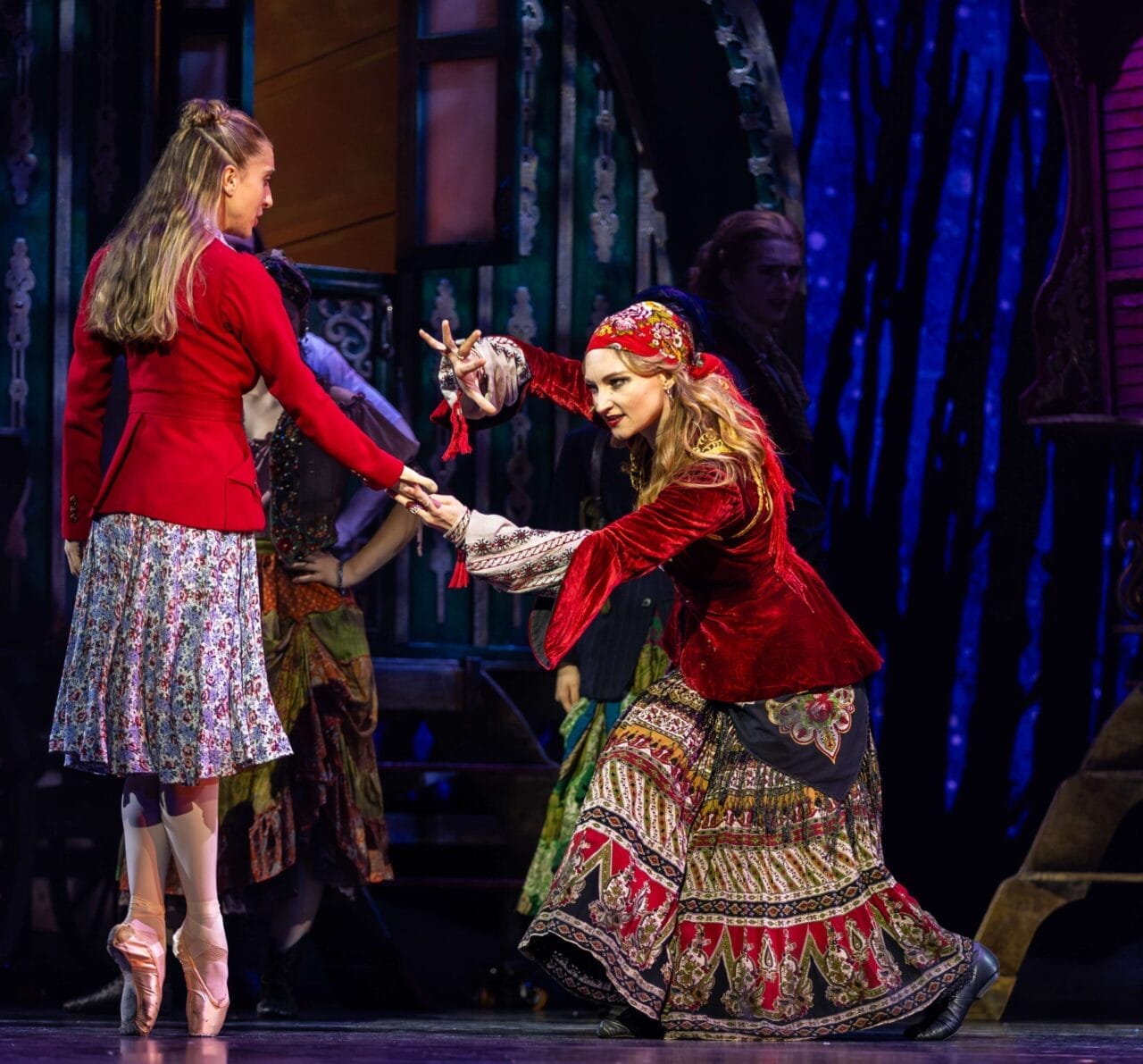 Two women in colorful costumes perform on stage; one stands while the other leans forward with dramatic hand gestures, bringing The Snow Queen to life against a theatrical backdrop.