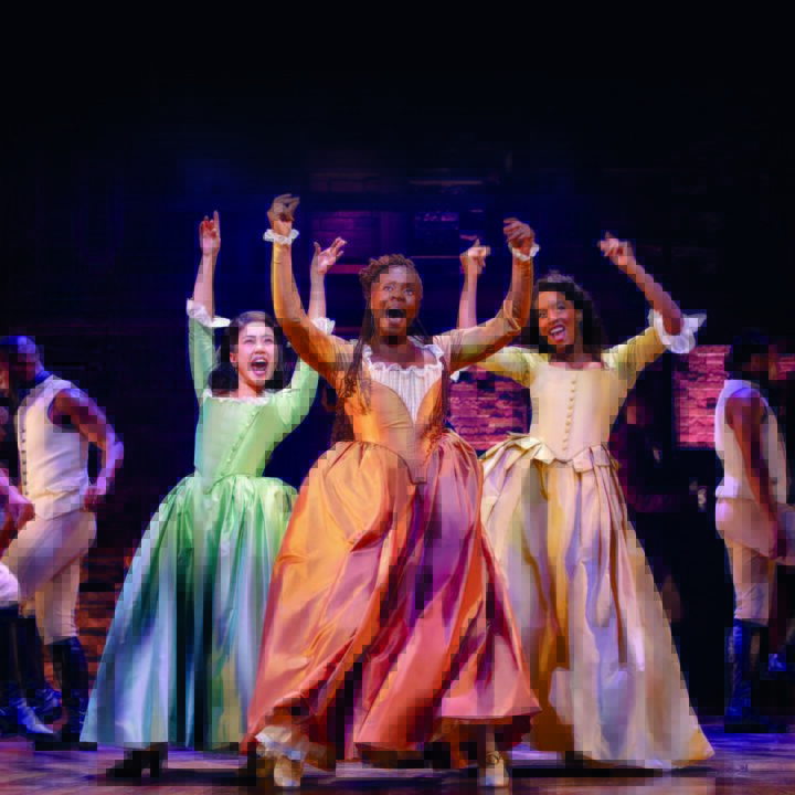 Performers on stage in period costumes, dancing energetically under bright lights.