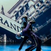 Two performers on stage, one dipping the other backward in a striking Mod Ballet pose, with a projected image of a building as the backdrop—evoking the bold spirit of Quadrophenia.