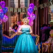 A woman in a turquoise gown sings at a lively indoor party decorated with purple balloons and a "Happy Birthday Boss" banner.