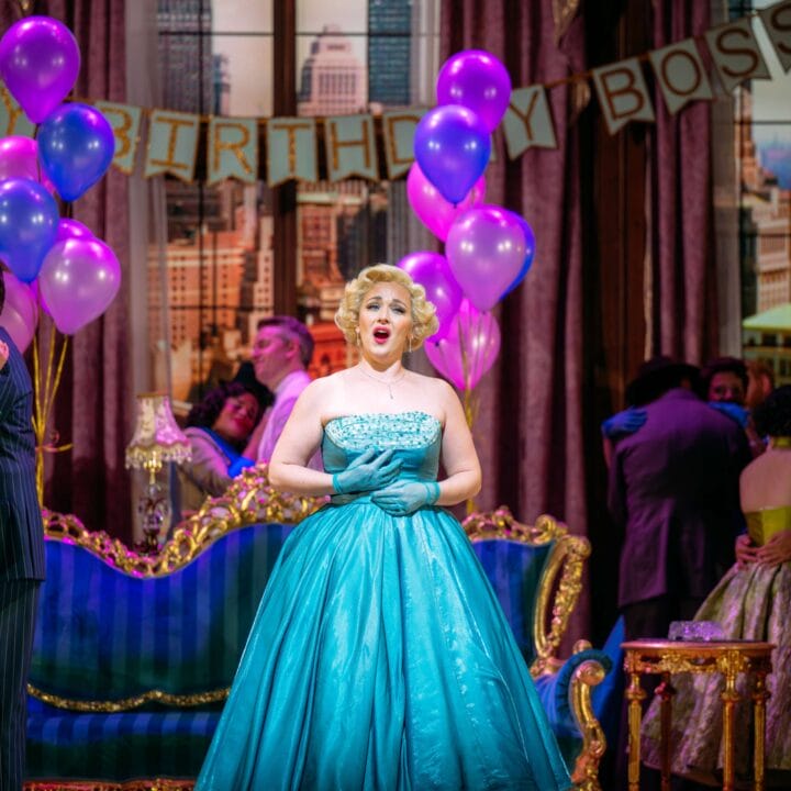 A woman in a turquoise gown sings at a lively indoor party decorated with purple balloons and a "Happy Birthday Boss" banner.