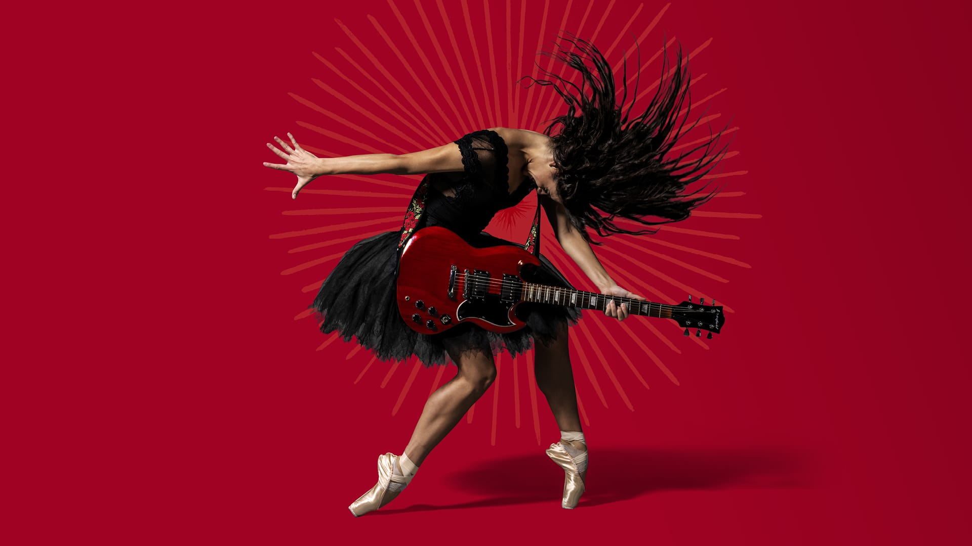 A woman wearing a black dress and pointe shoes plays an electric guitar while striking a dynamic pose against a red background with radiating lines.
