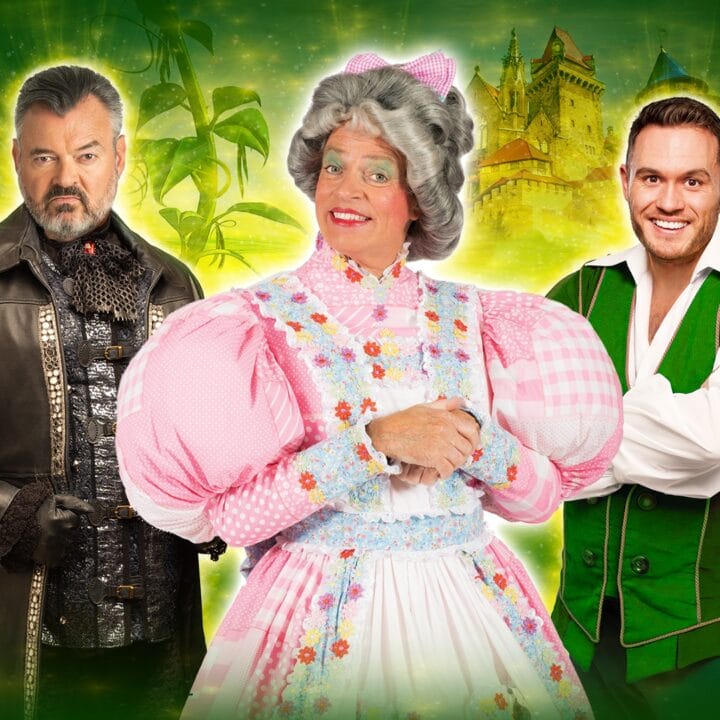 Three people in costume pose in front of a green, fantasy-themed background: one in a dark coat, one in a pink plaid dress and wig, and one in a green vest and white shirt.