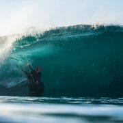 A surfer rides inside the barrel of a large, curling ocean wave under clear sky, illuminated by sunlight—capturing the spirit of adventure seen at the Ocean Film Festival.