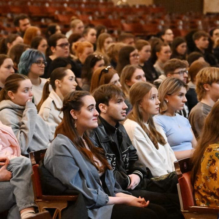 A diverse group of people sitting attentively in rows of auditorium seats, facing forward.