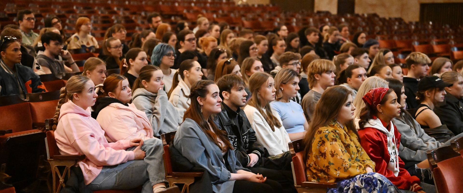A diverse group of people sitting attentively in rows of auditorium seats, facing forward.