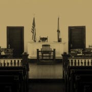 Empty courtroom with wooden benches, a judge’s bench, jury seats, and American and state flags in the background.