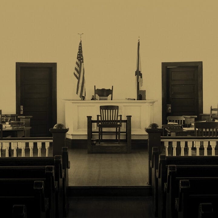 Empty courtroom with wooden benches, a judge’s bench, jury seats, and American and state flags in the background.