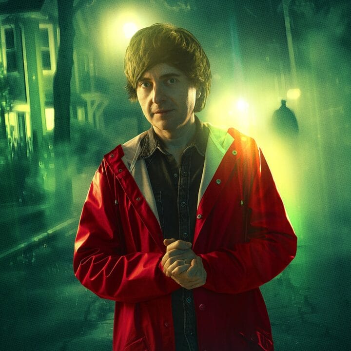 A man in a red raincoat stands on a dimly lit street at night, with greenish streetlights and a shadowy figure in the background.