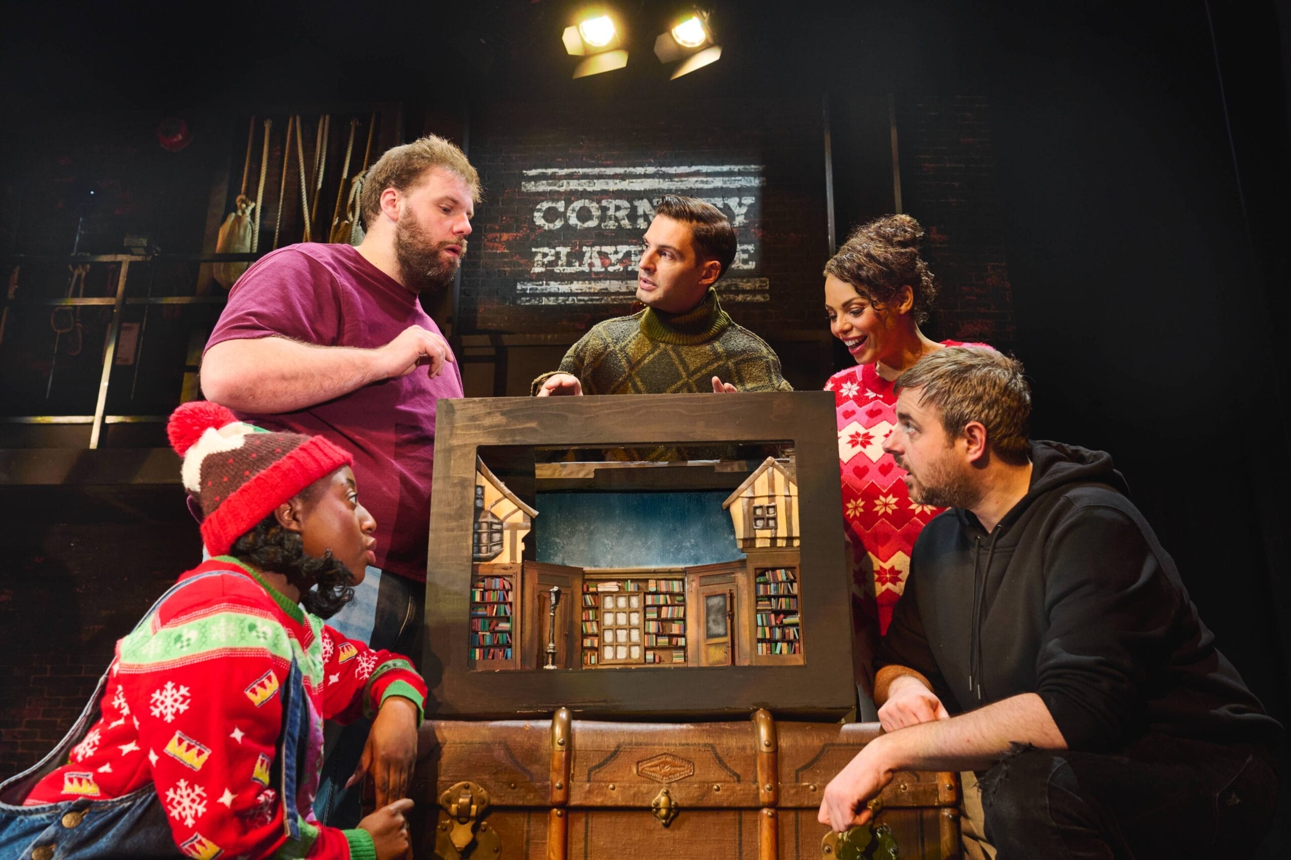 A group of people looking at a picture of a house, preparing for their Christmas Play that’s inspired by the classic Christmas Carol.