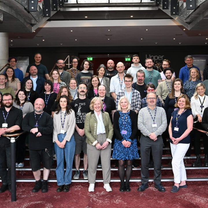 The staff of capital theatres pose together on indoor stairs for a group photo. Most are wearing lanyards and casual to business-casual attire.
