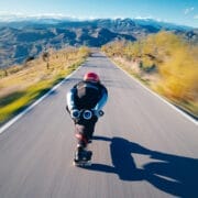 A person wearing a helmet and protective gear skateboards down a winding mountain road at high speed, participating in the Blue Programme, with blurred scenery indicating motion.