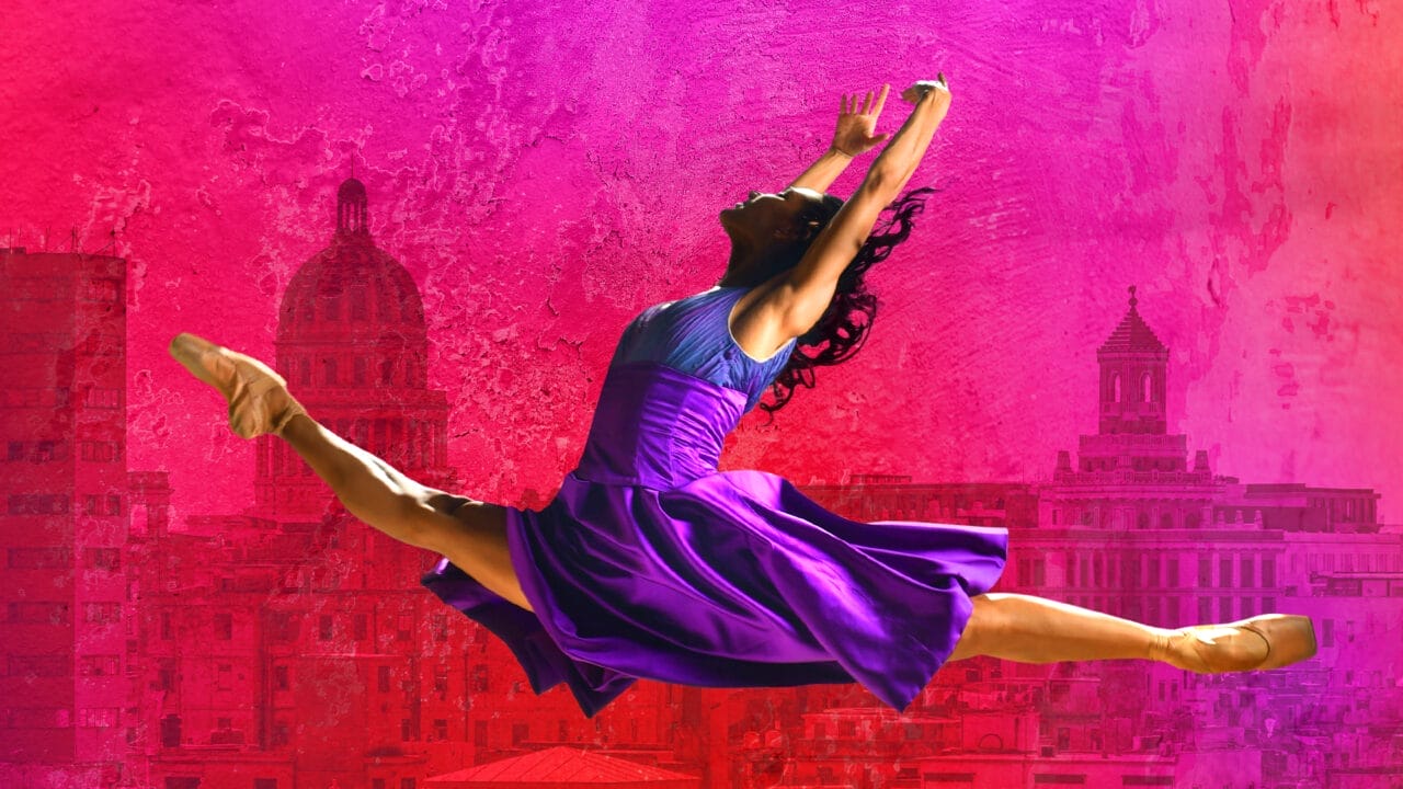 Ballet dancer in a purple dress performs a split leap against a vibrant pink and red cityscape background.