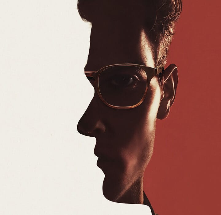 A man's face in profile is merged with a head-on portrait, divided by contrasting white and red backgrounds. The man wears glasses and looks serious.