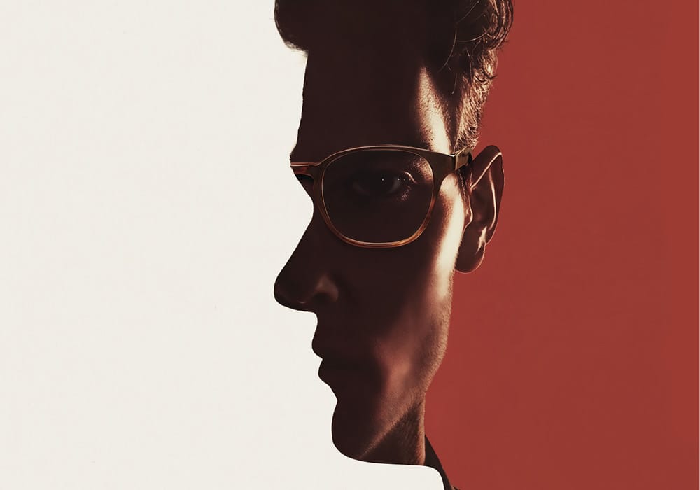 A man's face in profile is merged with a head-on portrait, divided by contrasting white and red backgrounds. The man wears glasses and looks serious.