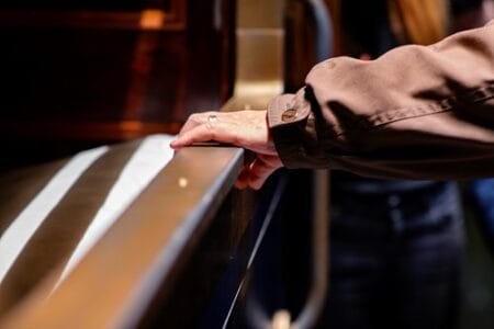 A hand resting on a banister in a theatre, adorned with a ring, against a blurred background.