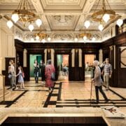 A spacious, ornate building lobby with marble floors, people walking and talking, a staircase on the left, large chandeliers, and decorative columns and ceiling moldings.