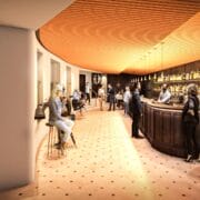 Modern bar interior with people sitting and standing, a curved wooden bar with shelves of bottles, warm lighting, and a mix of social interactions in a spacious setting.