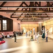 Children and adults gather in a spacious room with exposed wooden beams, large windows, mirrors, and seating areas; some play games while others sit or talk.