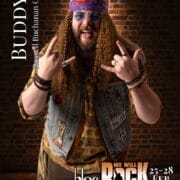 A man with long curly hair and a beard wears a bandana, sunglasses, a denim waistcoat with patches, and rings. He makes rock hand gestures and smiles. Text reads "BUDDY, Russell Buchanan Coid." Get ready for We Will Rock You event details!.
