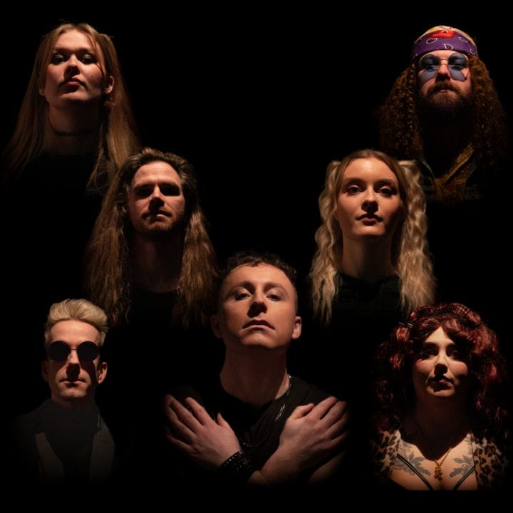 Seven people with serious expressions are positioned in a triangular arrangement against a black background, evoking the iconic "Bohemian Rhapsody" pose. Their faces are lit from below, casting dramatic shadows. The central person stands in front with arms folded.