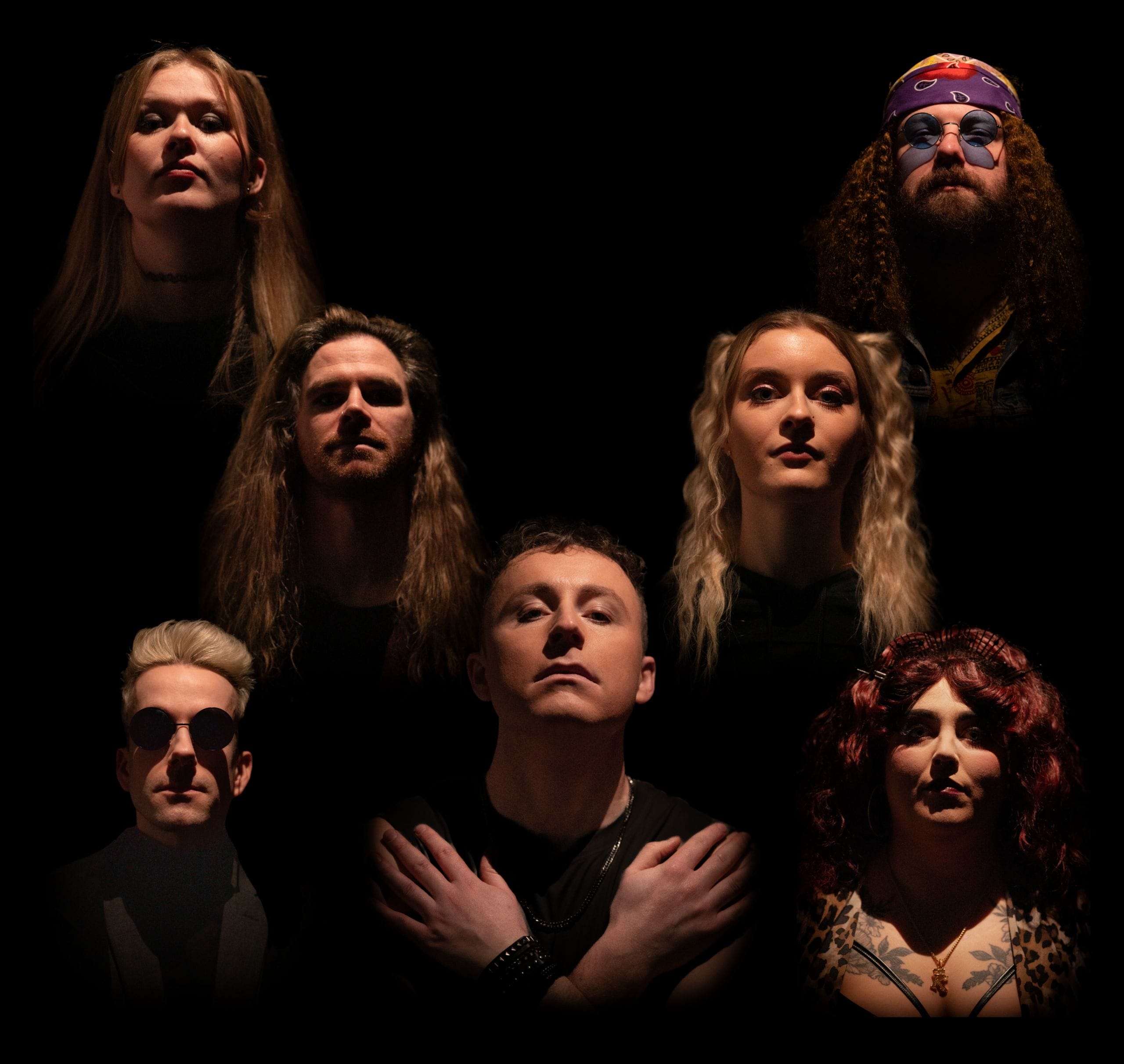 Seven people with serious expressions are positioned in a triangular arrangement against a black background, evoking the iconic "Bohemian Rhapsody" pose. Their faces are lit from below, casting dramatic shadows. The central person stands in front with arms folded.