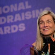 A woman stands at a podium smiling and holding an award, with a "National Fundraising Awards" sign in the background.