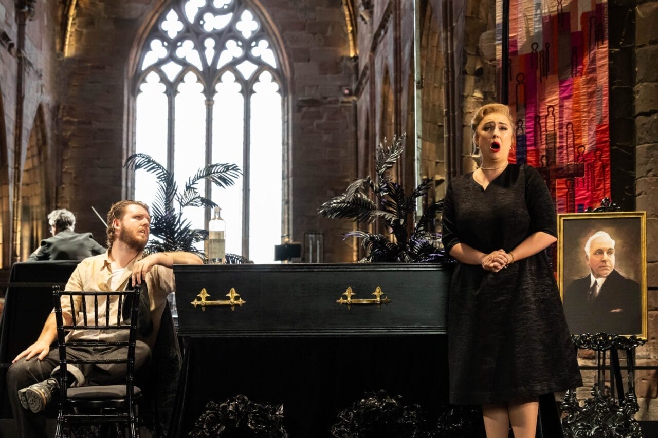 A woman sings beside a coffin and a portrait of an older man in a church, evoking the emotional depth of The Bear; a man sits nearby, watching her intently.