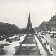 Black and white photo of a busy Princes Street with trams, pedestrians, and The Scott Monument at the center.