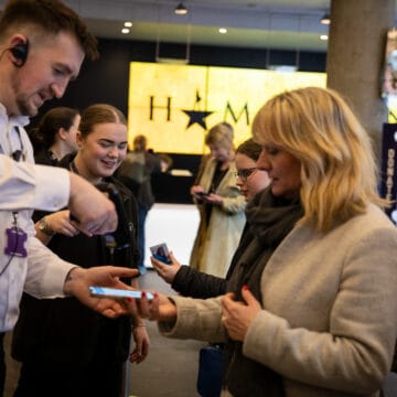 Staff scan a woman's ticket on her phone at the entrance to a theater with a "Hamilton" sign visible in the background.
