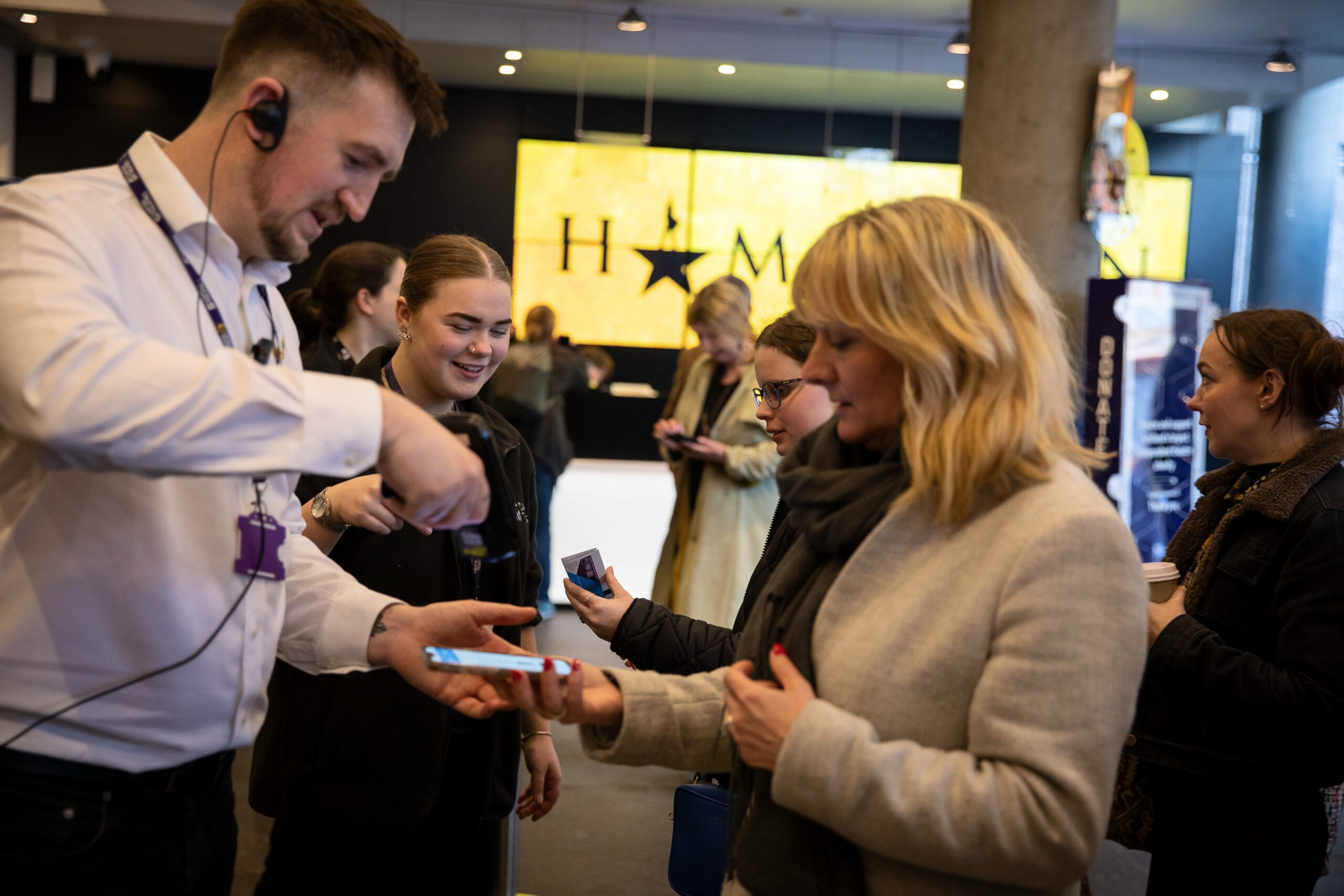 Staff scan a woman's ticket on her phone at the entrance to a theater with a "Hamilton" sign visible in the background.
