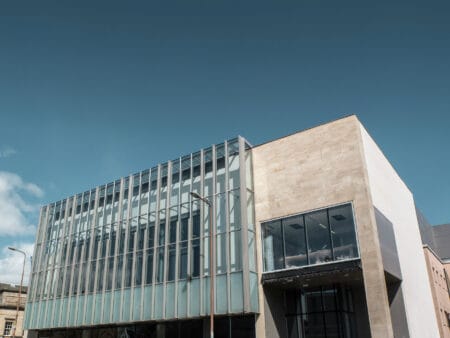Modern building with a glass façade and beige stone walls under a clear blue sky.