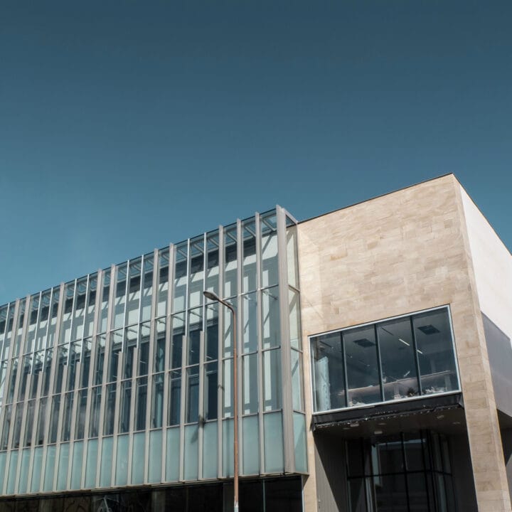 Modern building with a glass façade and beige stone walls under a clear blue sky.