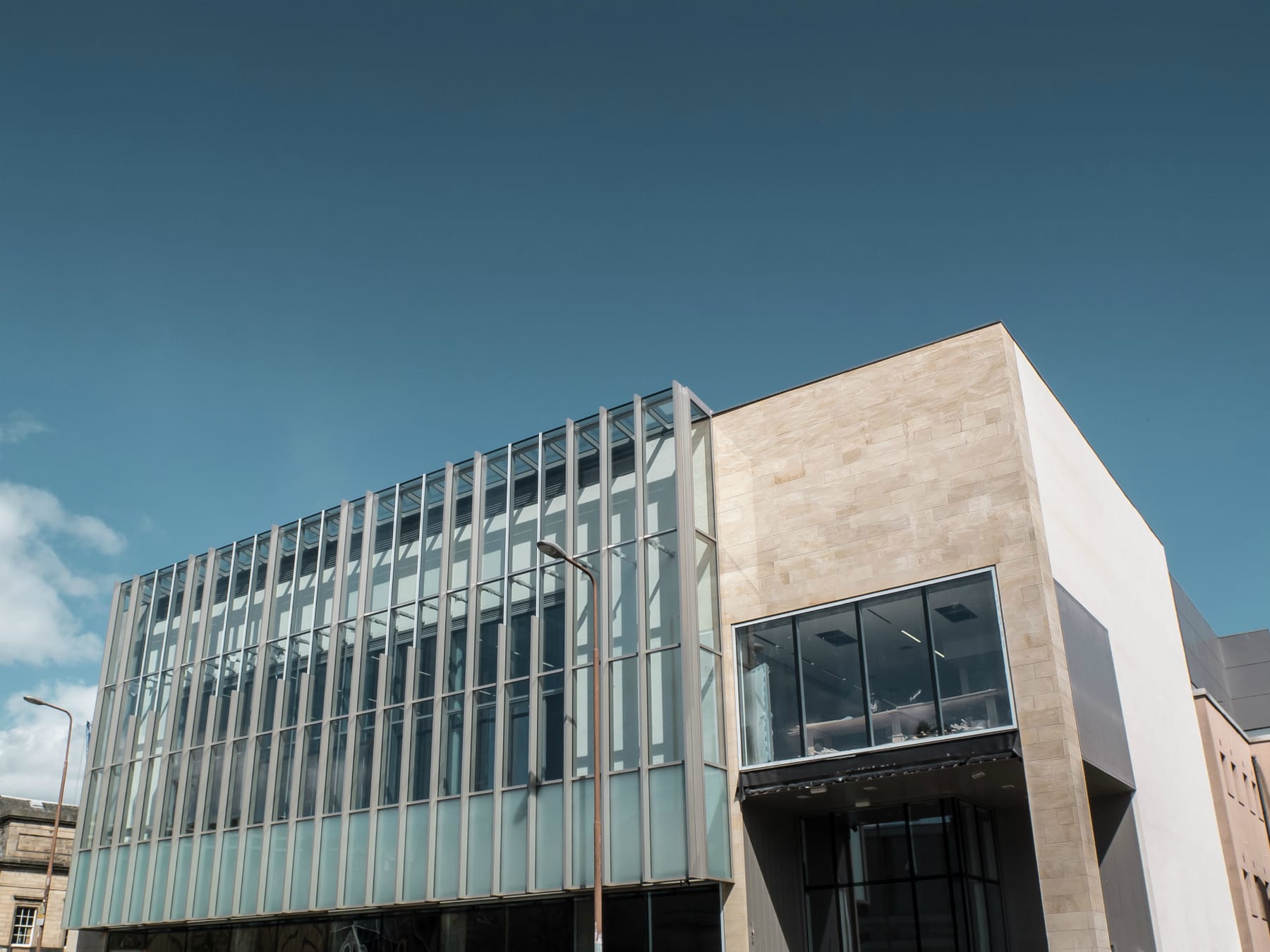 Modern building with a glass façade and beige stone walls under a clear blue sky.