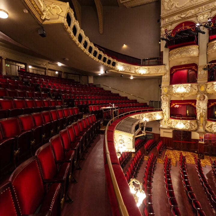 Empty rows of red velvet seats in the historic King's Theatre, showing ornate balconies and decorative architecture, viewed from the balcony level.