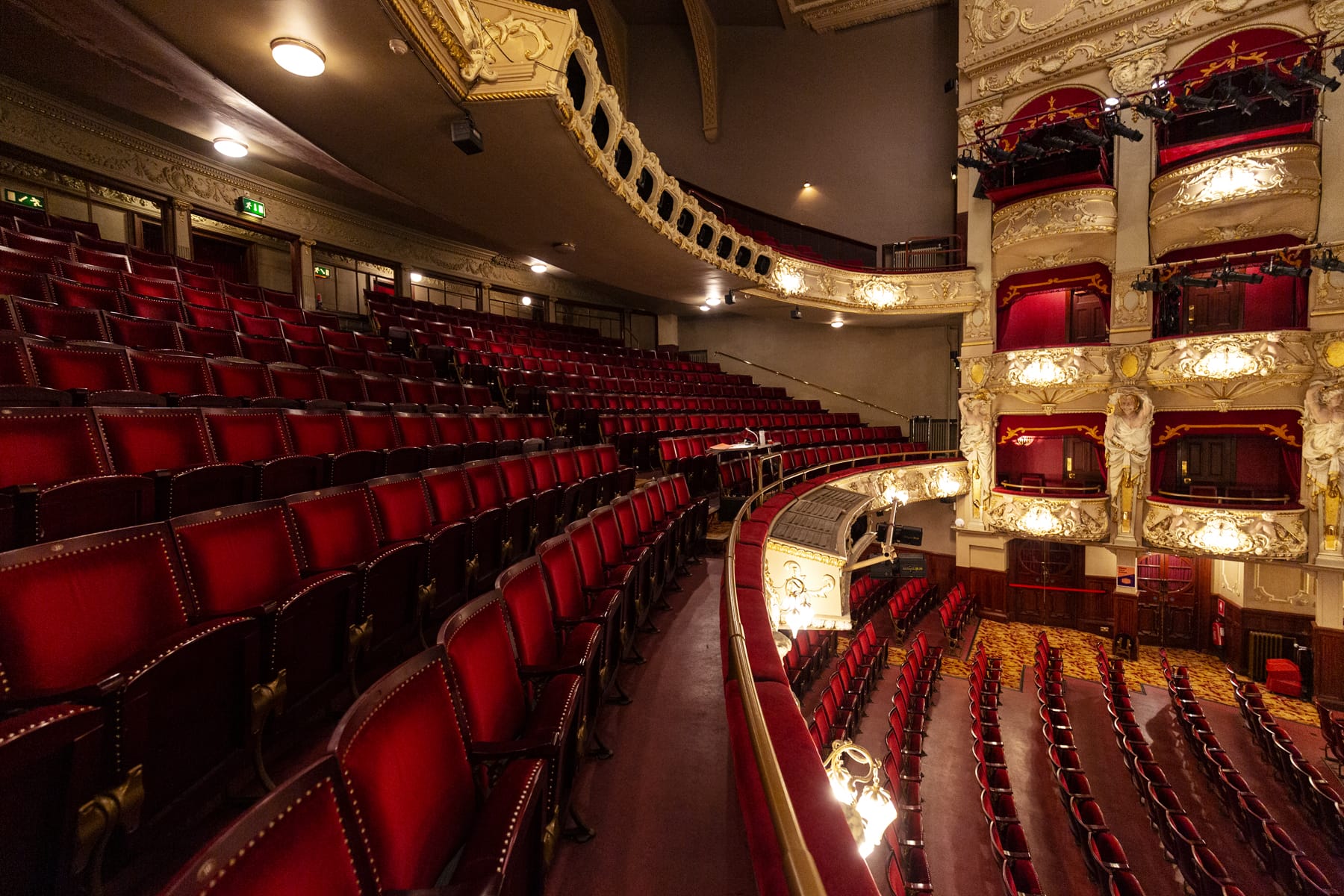 Empty rows of red velvet seats in the historic King's Theatre, showing ornate balconies and decorative architecture, viewed from the balcony level.