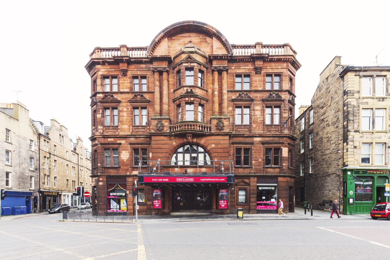 The King's Theatre, a historic, red sandstone building with arched windows and classical details sits on the corner of the a street in Tollcross, Edinburgh.