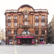 The King's Theatre, a historic, red sandstone building with arched windows and classical details sits on the corner of the a street in Tollcross, Edinburgh.