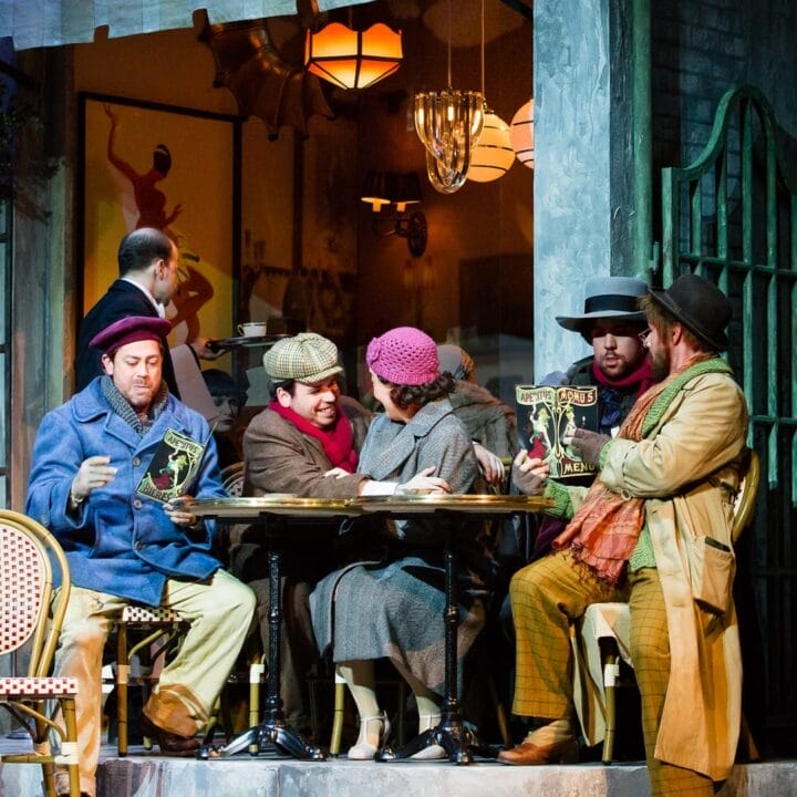 Five people in vintage attire sit at an outdoor café table, reading papers, with a waiter and another person visible inside the warmly lit restaurant.