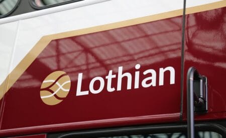 Side view of a maroon bus displaying the "Lothian" logo in white letters with a stylized gold emblem next to it.