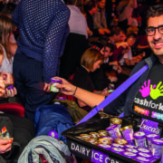 A man distributes small tubs of dairy ice cream from a tray to people seated in a crowded audience; one person wears noise-cancelling headphones.