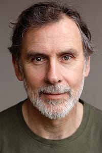 Middle-aged man with gray hair and beard, wearing a green crew-neck shirt, looking directly at the camera against a plain background.