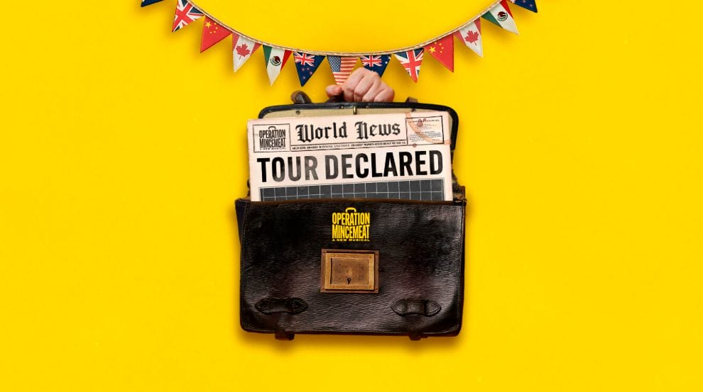 A hand holds a briefcase with a newspaper reading "Tour Declared" sticking out, against a yellow background with international flag bunting above.