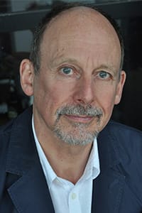 A middle-aged man with short hair, a beard, and mustache, wearing a white shirt and dark jacket, looking directly at the camera.