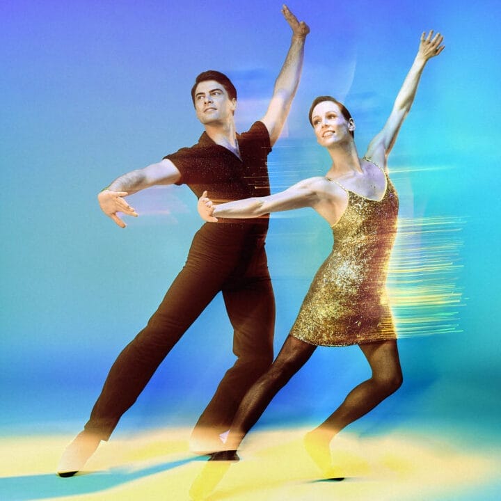 Two ballet dancers pose gracefully against a colorful, blurred background, with the female dancer in a gold dress and the male dancer in black attire.